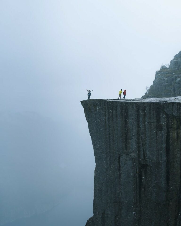 three persons standing near the edge of a cliff during day