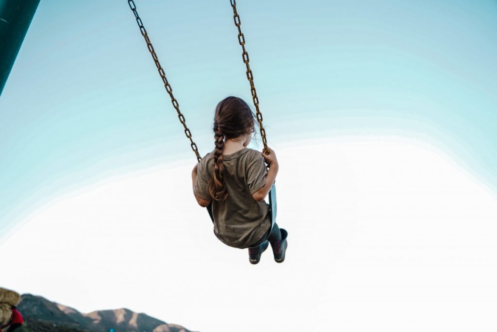 child in brown jacket sitting on swing during daytime