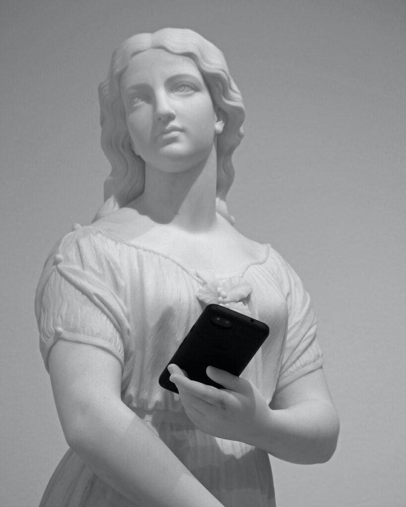 Low angle of stone classic statue with perfect skin and wavy hair holding modern cellphone near wall