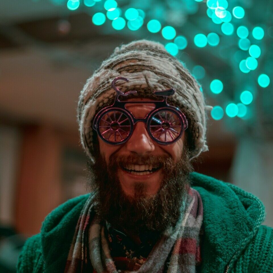 selective focus photography of man wearing gray knit cap, red-and-gray scarf and green cable knit zip hoodie