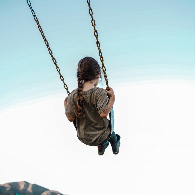 child in brown jacket sitting on swing during daytime