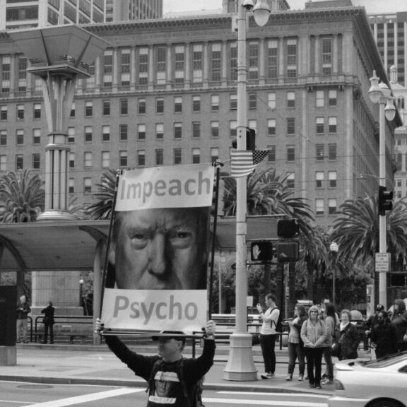 greyscale photography of man standing on road holding psycho banner