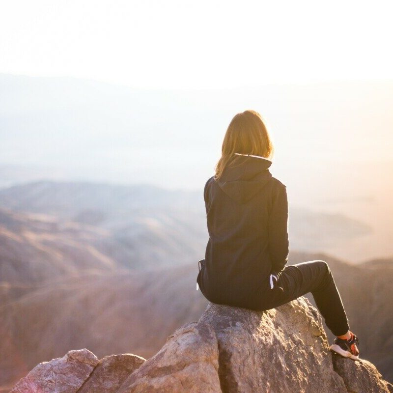 person sitting on top of gray rock overlooking mountain during daytime